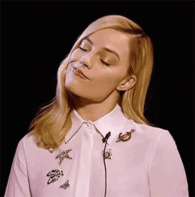 A Woman Is Wearing A White Shirt With Brooches On It And A Microphone In Her Neck . GIF