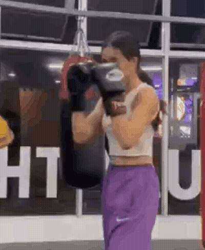 A Woman Is Wearing Boxing Gloves And Purple Pants In A Gym . GIF