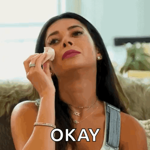 A Woman Is Wiping Her Face With A Napkin And The Word Okay Is On The Bottom . GIF
