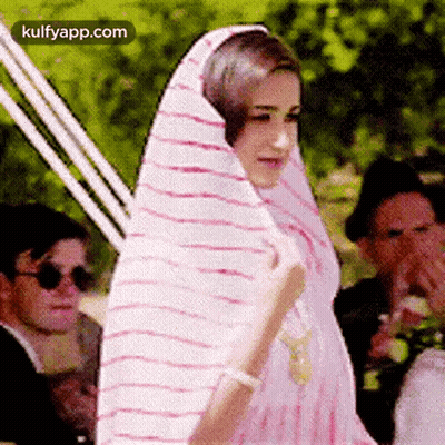 A Woman Is Wrapped In A Pink And White Striped Shawl . GIF