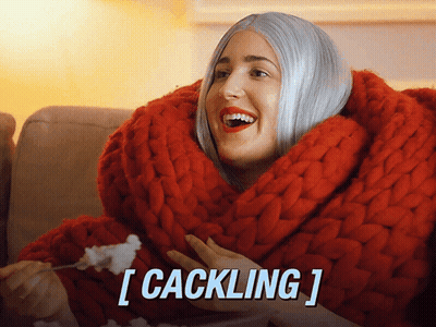 A Woman Is Wrapped In A Red Blanket And Eating Popcorn With The Caption [ Cackling ] GIF