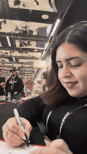 A Woman Is Writing On A Piece Of Paper With A Sharpie Marker While Wearing A Lanyard That Says Dmpack GIF