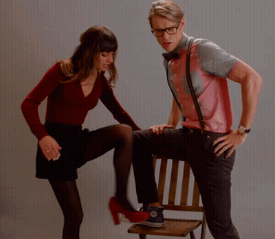 A Woman Kicking A Man 'S Leg Who Is Sitting In A Chair GIF