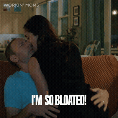 A Woman Kissing A Man On A Couch With The Words " I 'M So Bloated " GIF