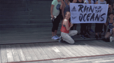A Woman Kneeling Down Holding A Banner That Says Run For The Oceans GIF