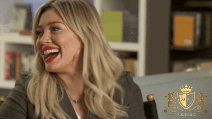 A Woman Laughs In Front Of A Shield That Says Mk On It GIF
