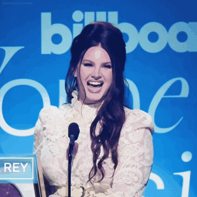 A Woman Laughs In Front Of A Sign That Says Billboard One GIF