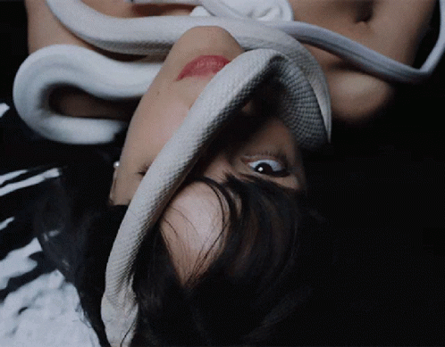 A Woman Laying Down With A Snake Around Her Face GIF