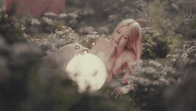 A Woman Laying In A Field Of Flowers Holding A Light GIF