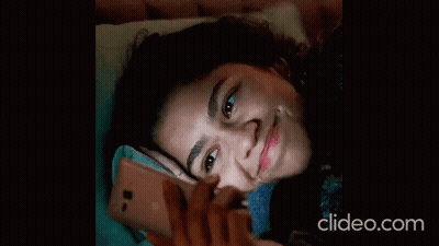 A Woman Laying On A Bed Looking At Her Phone With Clideo.com Written On The Bottom GIF