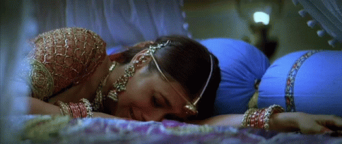 A Woman Laying On A Bed With A Blue Pillow Behind Her GIF