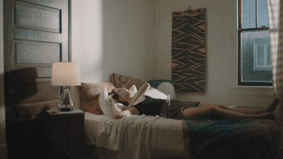 A Woman Laying On A Bed With A Lamp And A Window Behind Her GIF