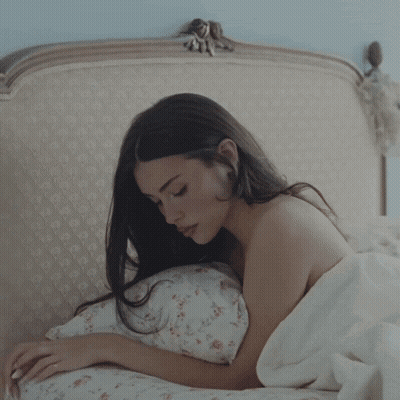 A Woman Laying On A Bed With A White Blanket GIF