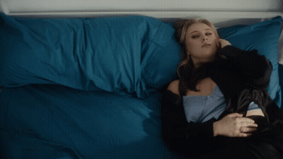 A Woman Laying On A Bed With Blue Pillows GIF