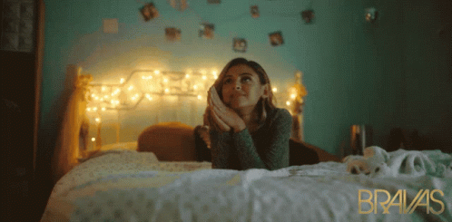 A Woman Laying On A Bed With Bravas Written In Gold GIF