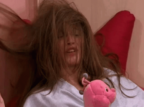 A Woman Laying On A Bed With Her Hair Blowing In The Wind Holding A Stuffed Pig GIF
