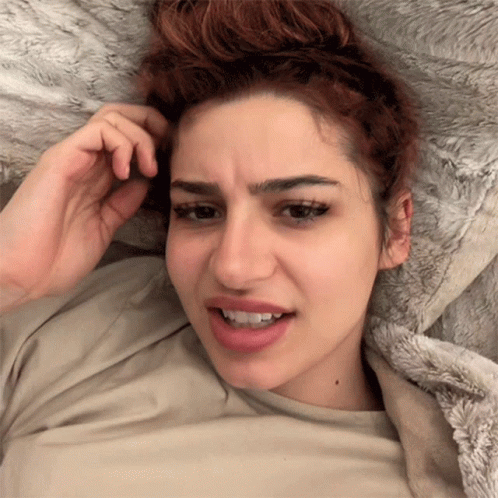 A Woman Laying On A Bed With Her Hand In Her Hair Making A Funny Face GIF
