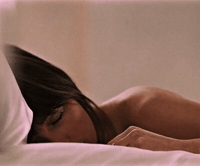 A Woman Laying On A Bed With Her Head On The Pillow GIF