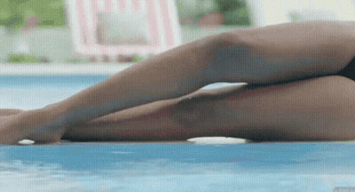 A Woman Laying On The Edge Of A Pool With Her Legs Crossed GIF