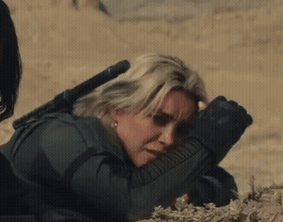 A Woman Laying On The Ground With A Rifle In Her Hand GIF