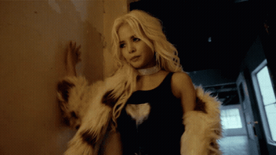 A Woman Leaning Against A Wall Wearing A Fur Coat And A Choker GIF