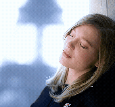 A Woman Leaning Against A Wall With Her Eyes Closed And A Badge On Her Shirt That Says ' Tommy Hilfiger ' GIF