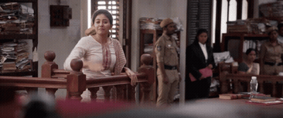 A Woman Leans On A Railing In A Courtroom While A Police Officer Stands In The Background GIF