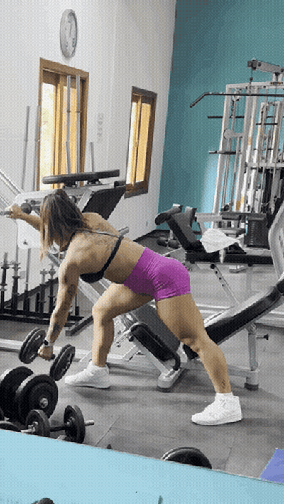 A Woman Lifting A Dumbbell In A Gym With A Clock On The Wall GIF