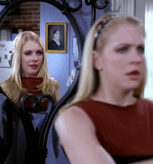 A Woman Looking At Herself In A Mirror With A Picture Of A Woman On The Wall Behind Her GIF