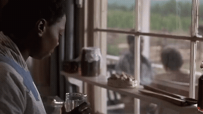 A Woman Looking Out Of A Window With A Glass In Her Hand GIF