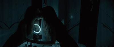 A Woman Looks At Her Reflection In A Mirror With A Light Ring GIF