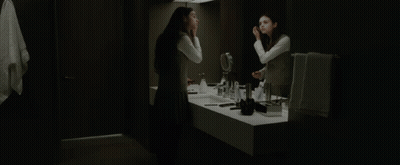 A Woman Looks At Herself In A Bathroom Mirror GIF