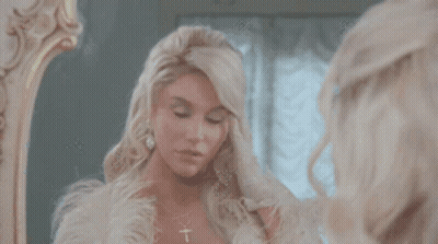 A Woman Looks At Herself In A Mirror And Adjusts Her Hair GIF