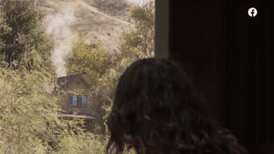 A Woman Looks Out A Window At A House With Smoke Coming Out Of It GIF