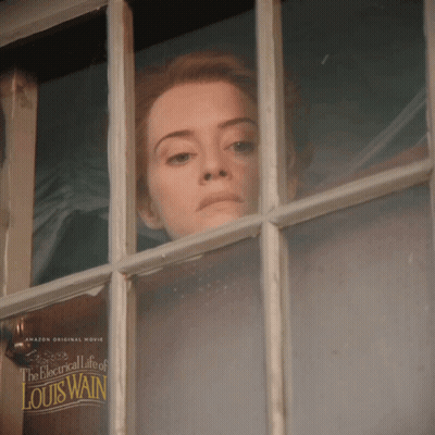 A Woman Looks Out A Window With A Poster For The Electrical Life Of Louis Wain GIF