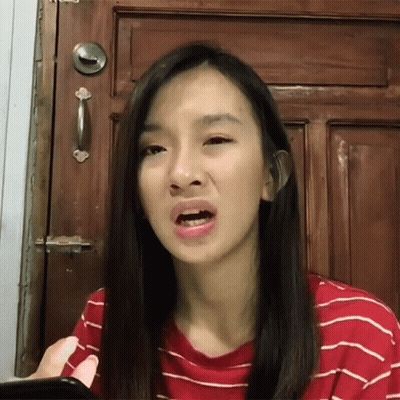 A Woman Making A Funny Face While Holding A Cell Phone In Front Of A Wooden Door GIF