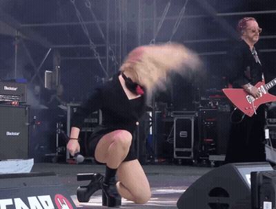A Woman On Stage With A Microphone In Front Of A Blackstar Guitar Amplifier GIF