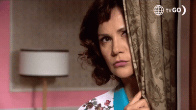 A Woman Peeking Out From Behind A Curtain With Tvgo Written On The Bottom Right GIF