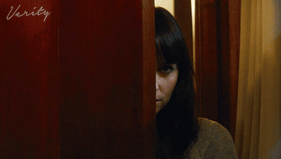 A Woman Peeking Out From Behind A Door With The Word Verity Written On It GIF