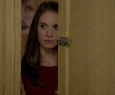 A Woman Peeking Out Of A Door With A Serious Look On Her Face GIF