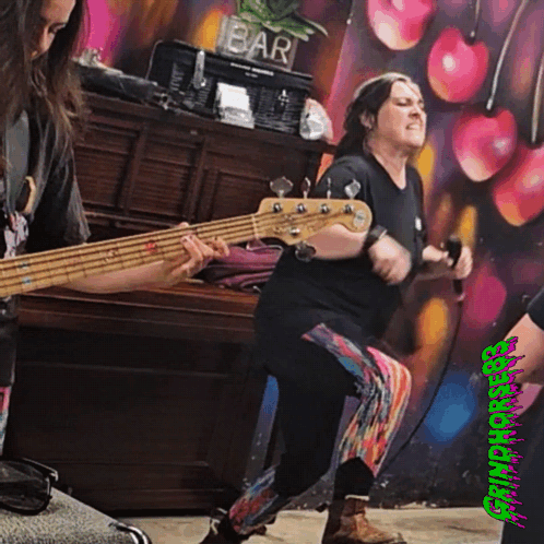 A Woman Playing A Bass Guitar In Front Of A Bar GIF