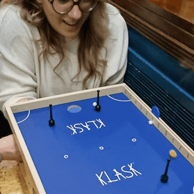 A Woman Playing A Game Called Klask On A Blue Board GIF