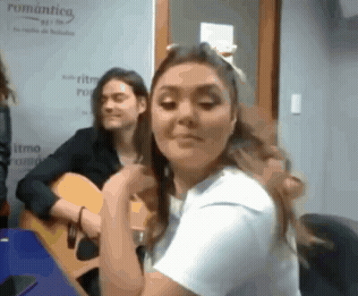 A Woman Playing A Guitar In Front Of A Sign That Says " Romantica " GIF