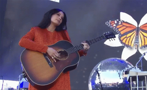 A Woman Playing An Acoustic Guitar In Front Of A Disco Ball GIF
