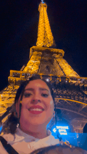 A Woman Poses In Front Of The Eiffel Tower At Night GIF