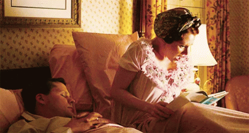 A Woman Reading A Book While A Man Sleeps GIF