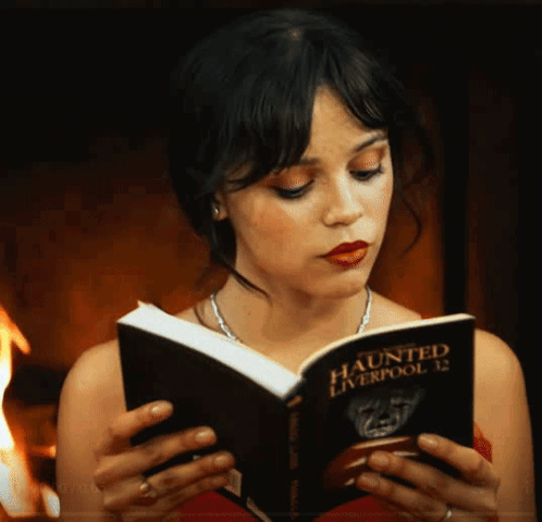 A Woman Reads A Book Titled Haunted Liverpool 12 GIF