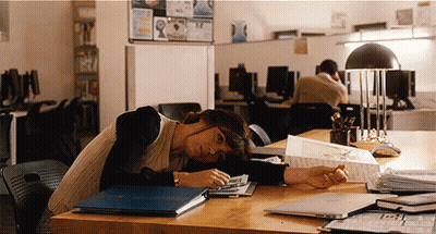 A Woman Rests Her Head On A Desk With A Blue Folder On It That Says ' A ' On It GIF
