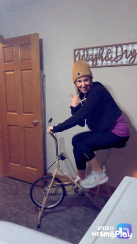 A Woman Riding A Bike In Front Of A Sign That Says Wash & Dry GIF