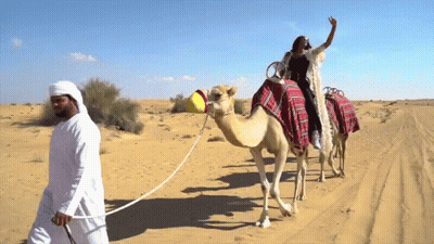 A Woman Riding On The Back Of A Camel Being Pulled By A Man GIF